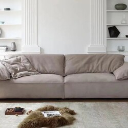 Sofa băng ba chỗ ngồi màu nâu be nhạt, đặt chính diện trong phòng khách hiện đại. Ghế có kiểu dáng tối giản, đệm ngồi và t…
