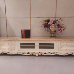 Kệ tivi tân cổ điển KT622-24 màu trắng ngọc trai với mặt đá hồng ngọc long nhân tạo, được chụp chính diện trong không gian…