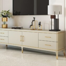 Kệ tivi mặt gỗ phong cách Mỹ, chụp chính diện trong không gian phòng khách hiện đại. Kệ có màu trắng kem chủ đạo với các đ…