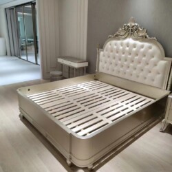 Giường ngủ 1m8 phong cách tân cổ điển, chụp từ góc chếch. Đầu giường bọc da nhân tạo màu kem, chần nút, kết hợp chạm khắc…