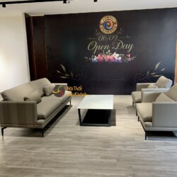 Bộ sofa SB86029T-113 gồm một băng dài và một băng đơn, bố trí đối xứng quanh bàn trà mặt đá trắng chân đen, trong showroom…