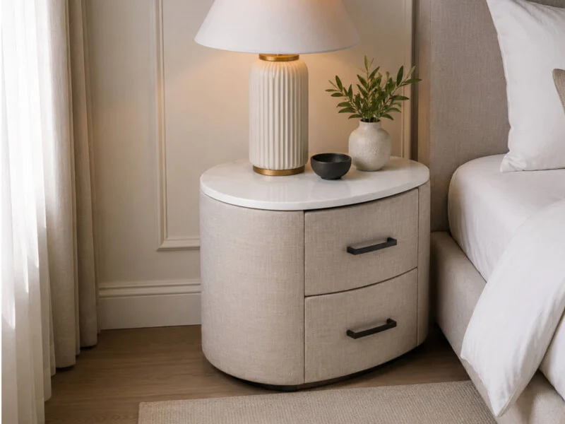 Góc chụp cận cảnh tủ đầu giường TA1807 đặt bên cạnh giường ngủ. Tủ có thiết kế bo tròn mềm mại, mặt đá trắng và thân bọc v…