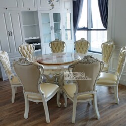 Bộ bàn ăn tròn 8 ghế phong cách tân cổ điển được chụp từ góc hơi chếch, cho thấy rõ mặt bàn đá vân hồng nhạt và chân bàn c…