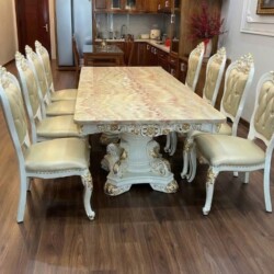 Bộ bàn ăn 10 ghế BAT66-24 chụp cận cảnh từ phía trước, đặt trên sàn gỗ. Bàn ăn mặt đá Hồng ngọc long nhân tạo với vân đá đ…