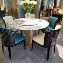 Bàn ăn tròn mặt đá phiến trắng vân xám với mâm xoay trung tâm, đặt trong không gian showroom sang trọng. Chân bàn hình trụ…