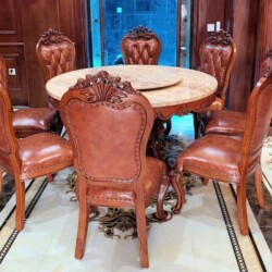 Bộ bàn ăn tròn tân cổ điển với 6 ghế được sắp xếp quanh bàn, chụp từ góc hơi chếch phía trước. Bàn có mặt đá màu vàng kem…