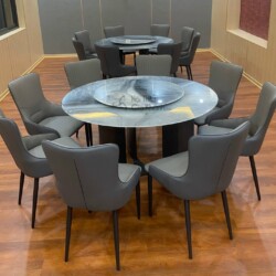 Bộ bàn ăn tròn hiện đại BA928-135 chụp chính diện, với mặt bàn đá vân xám đen có mâm xoay. Chân bàn trụ màu đen. Xung quan…