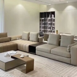 Bộ sofa góc chữ L hiện đại màu nâu nhạt, chụp từ góc chếch phía trước, đặt trong phòng khách sang trọng với tường trắng và…