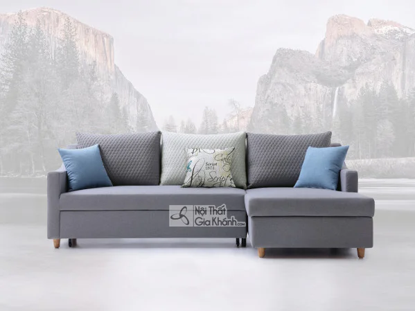 Một chiếc ghế giường sofa góc chữ L màu xám hiện đại, được chụp chính diện trên nền trắng với phông nền núi mờ ảo. Sofa có…