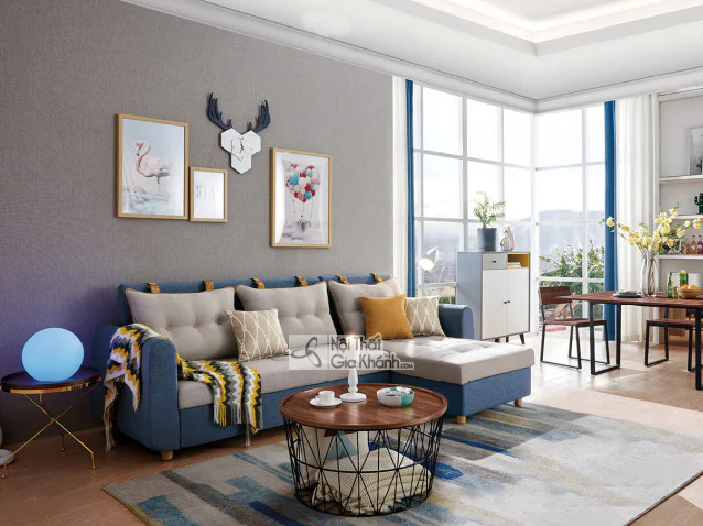 Sofa giường góc chữ L hiện đại bọc vải màu xanh dương và be, đặt trong phòng khách sáng sủa. Sofa có tựa lưng rút múi, đi…