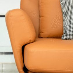 Cận cảnh tay vịn sofa da màu cam với đường may chắc chắn, mềm mại, bên cạnh là gối tựa trang trí họa tiết houndstooth đen…