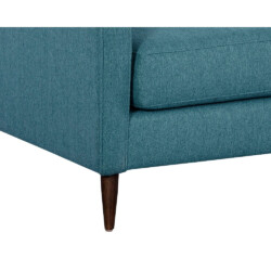 Cận cảnh chi tiết chân ghế sofa màu xanh ngọc, chụp từ góc thấp. Chân ghế làm bằng gỗ tự nhiên, có hình dáng côn thon dần…