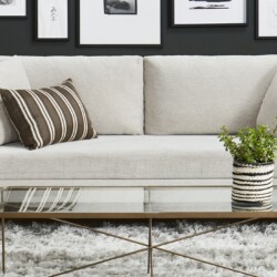 Sofa băng Ainsley SF-369 bọc vải màu be nhạt, đặt trong không gian phòng khách hiện đại với tường màu đen và các bức tranh…