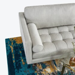 Góc nhìn từ trên xuống của sofa băng 3 chỗ bọc vải màu xám nhạt, đặt trên thảm họa tiết xanh và cam. Bố cục độc đáo, làm n…