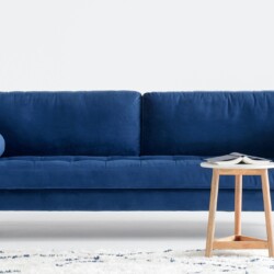 Sofa băng 3 chỗ bọc vải màu xanh navy nổi bật, đặt giữa phòng khách với thảm họa tiết và bàn trà gỗ nhỏ. Góc chụp chính di…