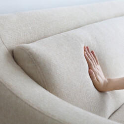 Cận cảnh tay vịn cong mềm mại của sofa SF-189 màu be nhạt, với bàn tay chạm nhẹ vào bề mặt vải. Hình ảnh làm nổi bật chất…