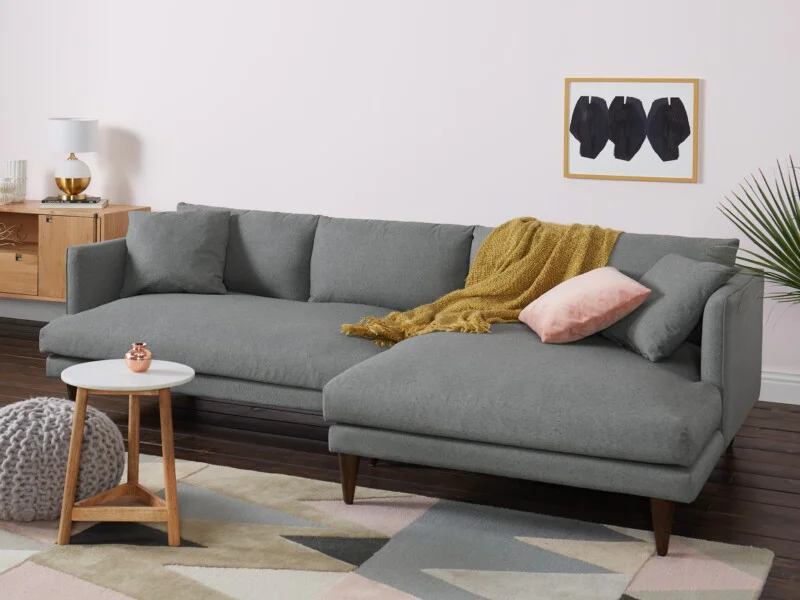 Sofa góc chữ L Lewis SF-489 bọc vải màu xám nhạt, đặt trong phòng khách hiện đại với tường hồng phấn. Sofa thiết kế tối gi…