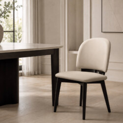 Ghế ăn LUMIÈRE GHY925 màu kem/be, chụp góc nghiêng nhẹ trong phòng ăn hiện đại. Ghế có lưng cong, đệm dày bọc da sinh thái…