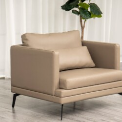 Ghế sofa đơn BM001-113-C1050 màu nâu be với đệm tựa lưng và gối ôm nhỏ, đặt trong không gian phòng khách có rèm trắng và c…