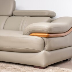 Cận cảnh tựa tay bo cong của sofa da màu be/ghi sáng, có chi tiết ốp gỗ màu nâu sáng. Chụp từ góc thấp, làm nổi bật đường…