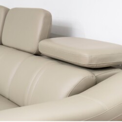 Cận cảnh phần tựa đầu điều chỉnh và góc nối của sofa da màu be/ghi sáng. Chụp từ góc trên xuống, làm rõ các đường may tinh…