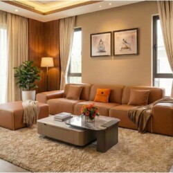 Sofa băng SFA38-32 ba chỗ ngồi và đôn đi kèm, bọc da bò màu nâu caramel, được đặt trong không gian phòng khách hiện đại. G…