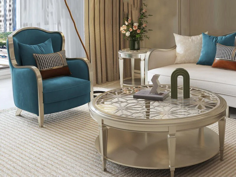 Ghế sofa đơn bọc vải màu xanh ngọc với khung gỗ sơn bạc, đặt cạnh bàn trà tròn mặt kính cường lực có họa tiết trang trí ti…