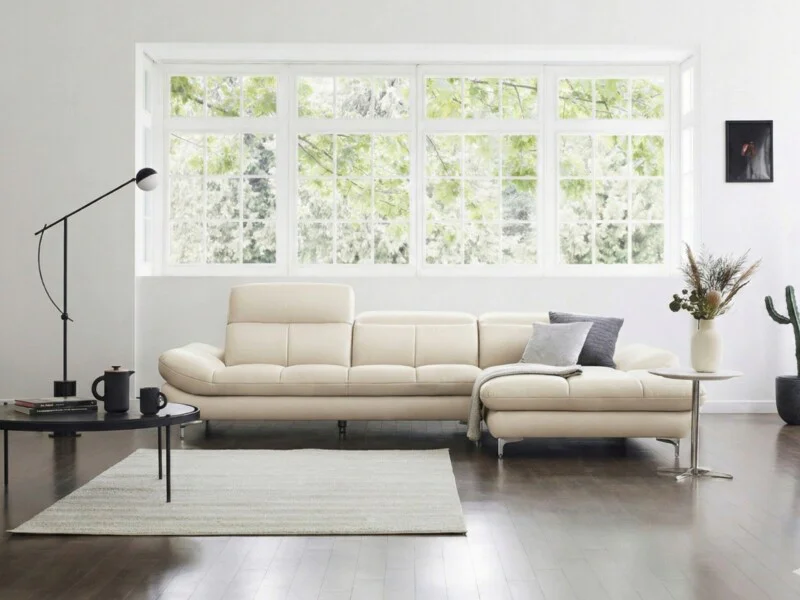 Sofa ASCEND kiểu dáng góc phải, màu kem ngả, được bố trí trong không gian phòng khách hiện đại với thảm lông màu xám và bà…