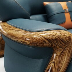 Cận cảnh tay vịn của băng sofa bọc da màu xanh ngọc, nổi bật với phần ốp gỗ mun tự nhiên có vân gỗ độc đáo, uốn lượn mềm m…