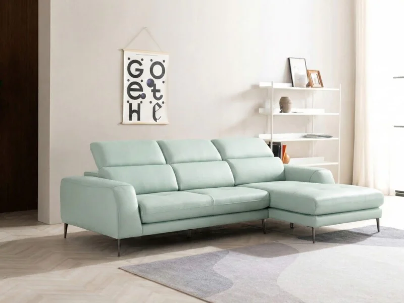 Sofa góc da màu xanh bạc hà nhạt, chụp toàn cảnh từ phía trước bên phải, đặt trong phòng khách hiện đại với tường trắng, k…