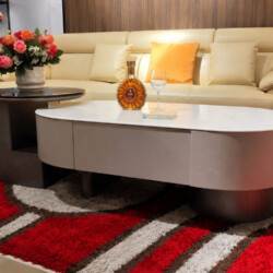 Bàn trà đôi LUNEA trong bối cảnh phòng khách sang trọng với sofa da màu kem, thảm đỏ họa tiết nổi bật. Trên bàn có bình ho…