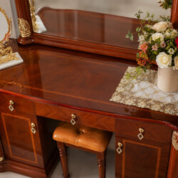Góc nhìn cận cảnh mặt bàn trang điểm màu nâu đỏ, bề mặt bóng loáng phản chiếu ánh sáng. Bàn có hai ngăn kéo nhỏ và một ngă…