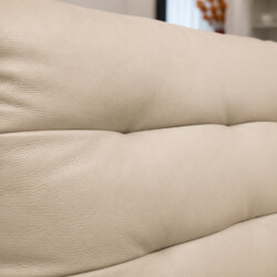 Cận cảnh bề mặt da bò tự nhiên của sofa AUREO màu kem nhạt, cho thấy rõ vân da mềm mại và độ bóng nhẹ. Các đường may tinh…