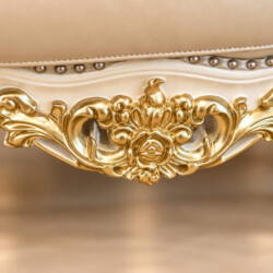 Chi tiết phần khung gỗ phía trước của ghế sofa, tập trung vào họa tiết chạm khắc nhũ vàng hình hoa lá cầu kỳ, mang đậm pho…