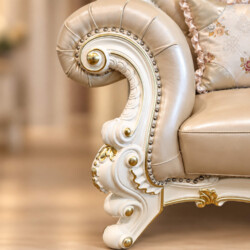 Cận cảnh tay vịn và chân ghế sofa, thể hiện rõ đường cong mềm mại của tay vịn bọc da bò tự nhiên màu be, điểm xuyết đinh t…