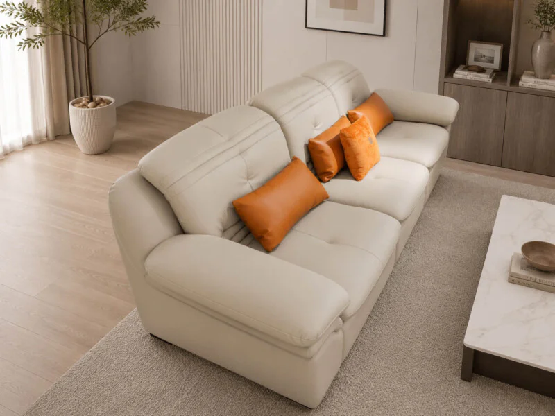 Sofa NEROX bọc da màu kem nhạt, chụp từ góc chéo bên phải, cho thấy tổng thể kiểu dáng chữ L nhẹ nhàng và các gối tựa màu…