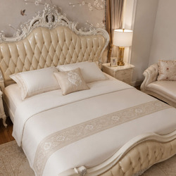 Cận cảnh giường ngủ MONARCHIA 1m8 từ góc thấp, tập trung vào đầu giường bọc da múi rút khuy màu kem/vàng nhạt và phần khun…