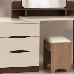 Cận cảnh phần bàn trang điểm LIVIA và ghế đôn đi kèm, góc chụp thấp. Tập trung vào chi tiết các ngăn kéo màu kem với tay n…