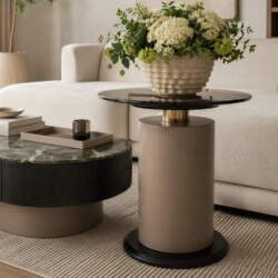 Cận cảnh bàn trà nhỏ ARDO hình trụ màu be với mặt kính đen bóng, đặt cạnh bàn trà lớn. Trên bàn nhỏ có bình hoa trắng lớn…