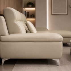 Sofa góc COASTAL II bọc da công nghiệp màu be nhạt, chụp từ góc ngang bên phải, cho thấy phần chaise dài và chân inox. Bối…